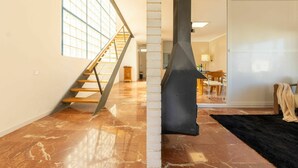 A spacious room with a marble floor, a wooden staircase, and a large window.