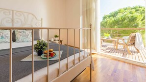 A bedroom with a bed, a small table with a plant, and a balcony with outdoor furniture.