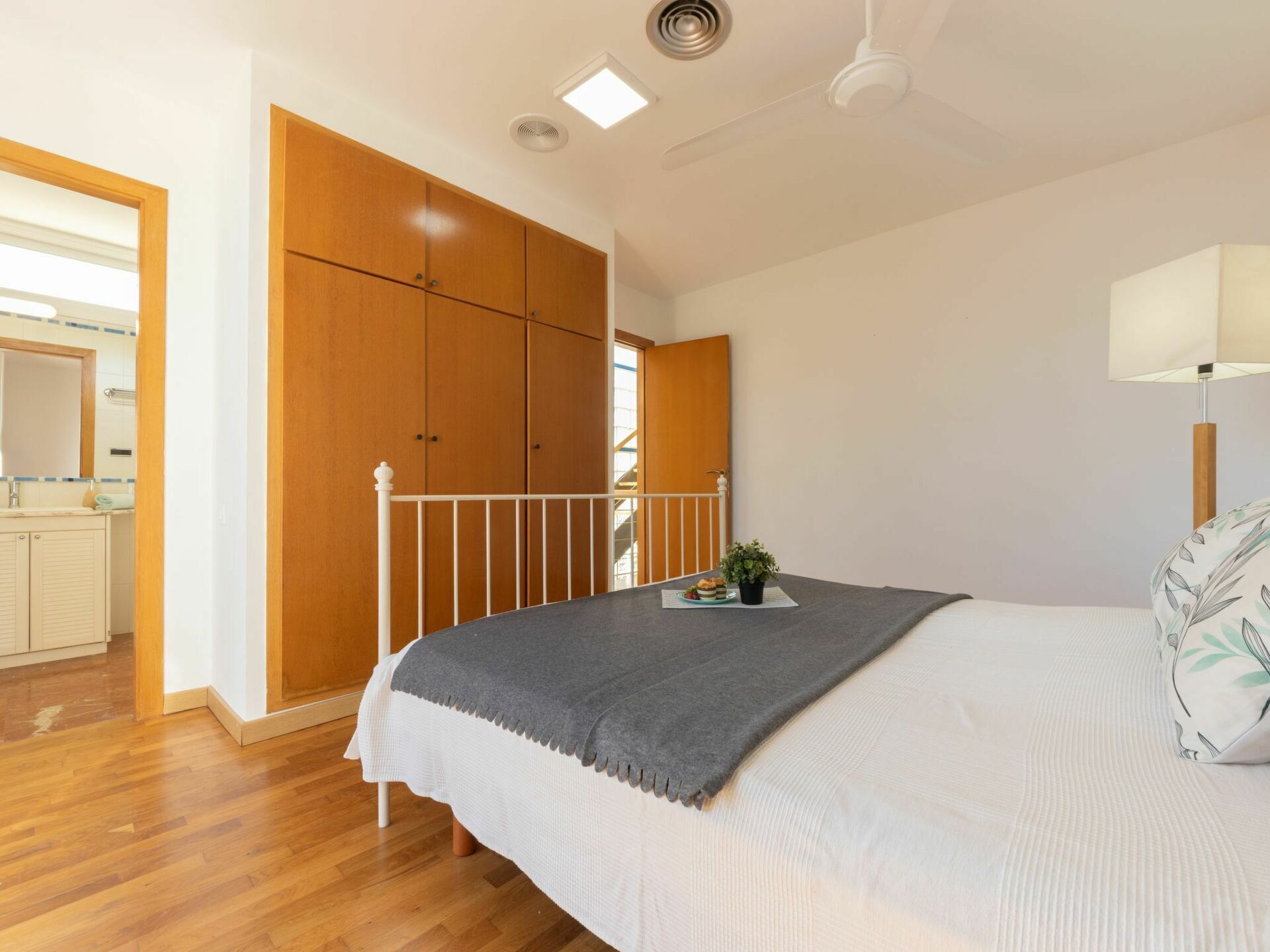 Une chambre à coucher comprenant un lit, une table de chevet, une lampe, une fenêtre et une vue sur une salle de bain et un escalier.