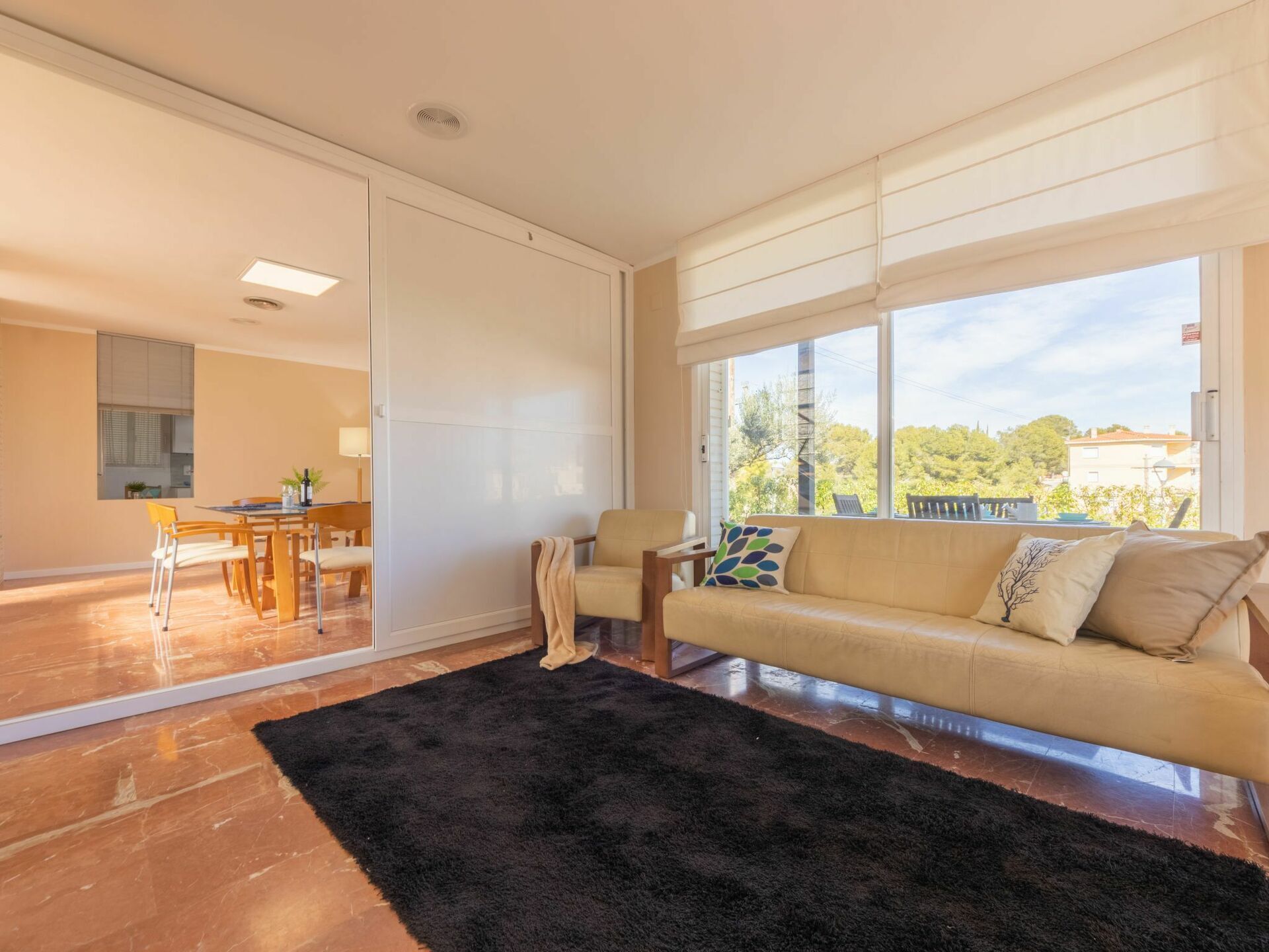 A spacious living room with a large window, a sofa, a coffee table, and a dining area.