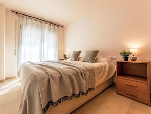 A bedroom with a bed, a nightstand, a lamp, and a potted plant.