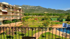 A balcony with a view of a landscaped garden, a pool, and a mountain in the background.