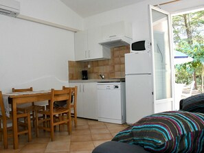 Eine kompakte Küche mit weißen Schränken, einem Geschirrspüler von Bosch und einer Mikrowelle. Ein Esstisch mit Stühlen und ein Fenster mit Blick auf die grüne Umgebung.