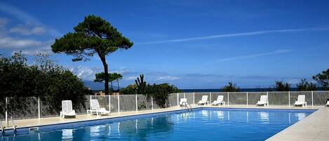 A rectangular swimming pool with a tiled deck, surrounded by white lounge chairs and a white fence.