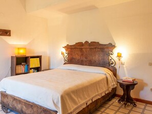 Un dormitorio con una cama de madera, una mesita de noche con lámpara, una estantería y un aplique de pared.