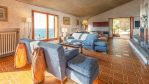 Amplia sala de estar con vista al mar, que incluye un juego de sofás, un tambor y una chimenea.