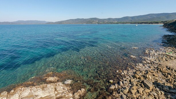 Una vista despejada del litoral con costa rocosa y montañas a lo lejos.