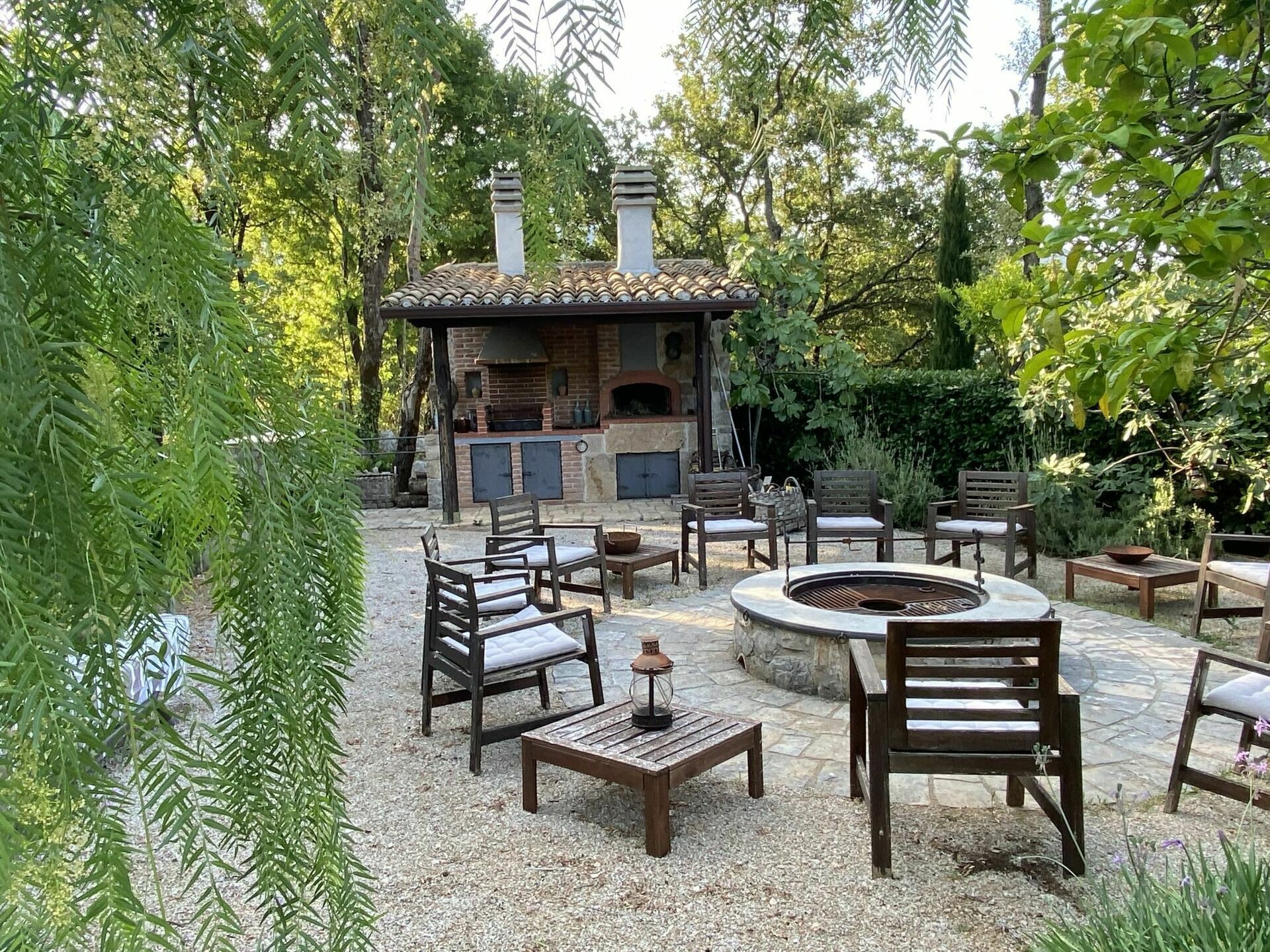 An outdoor patio with a stone fire pit, wooden seating, and a brick fireplace.