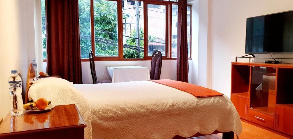 Habitación de hotel con una cama, un televisor sobre un mueble de madera y una ventana con cortinas.