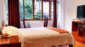 Habitación de hotel con una cama, un televisor sobre un mueble de madera y una ventana con cortinas.