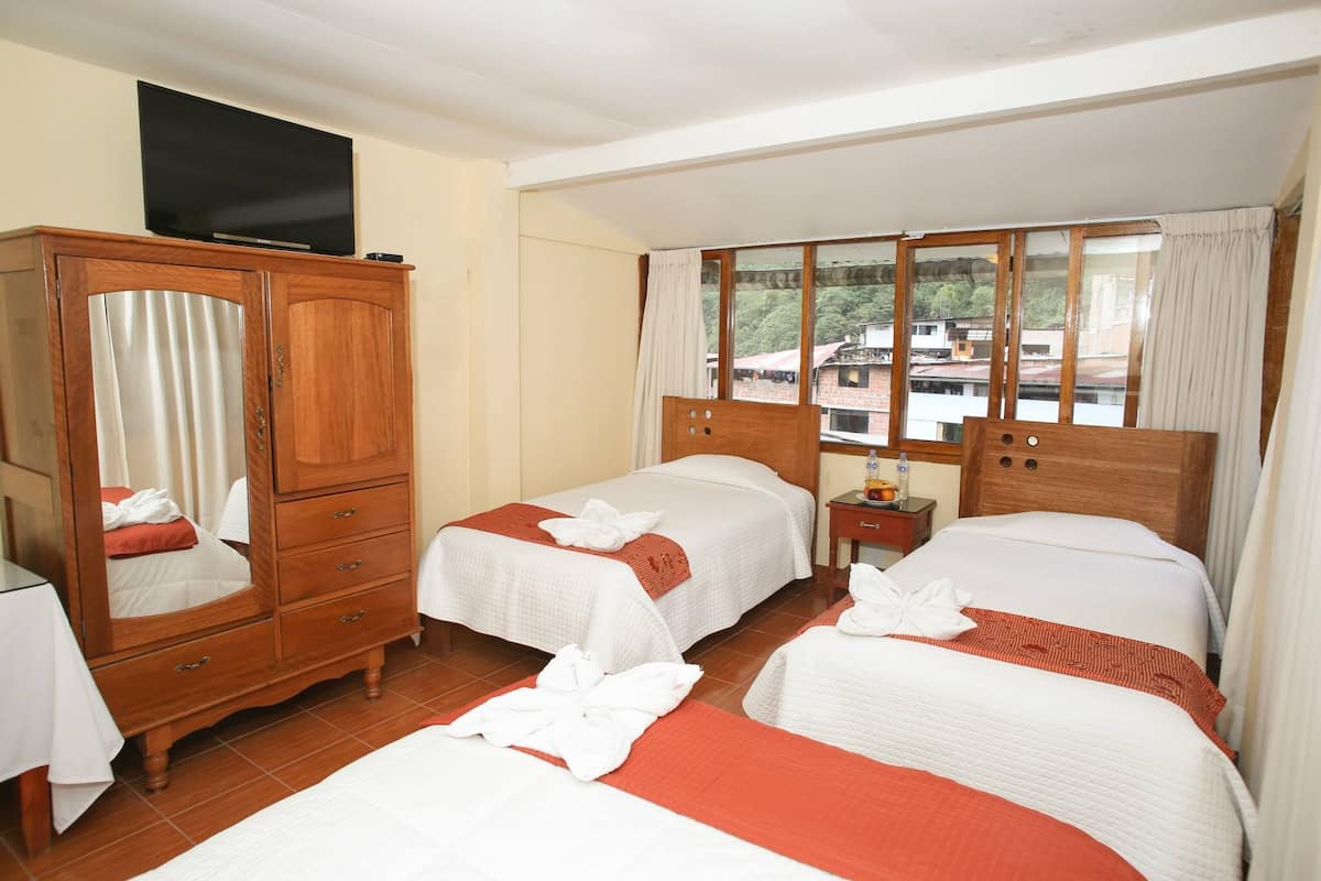 A hotel room with two beds, a wooden wardrobe, a television, and a window with a view of buildings.