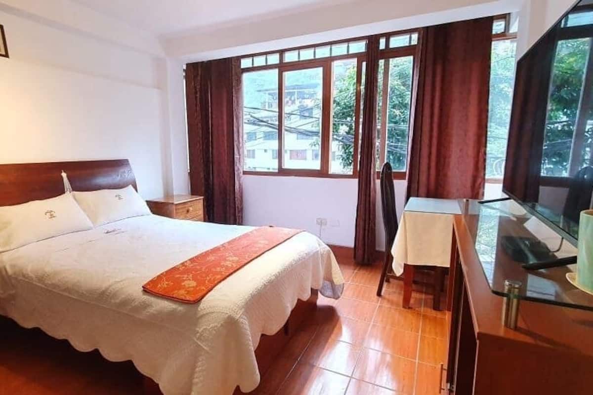 A hotel room with a bed, a desk, a chair, a lamp, and a window with curtains.
