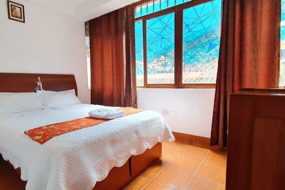 A bedroom with a wooden bed, white bedding, a wooden nightstand, and a window with curtains.