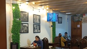 Een restaurant met houten tafels en stoelen, een televisiescherm en ingelijste foto’s aan de muur.