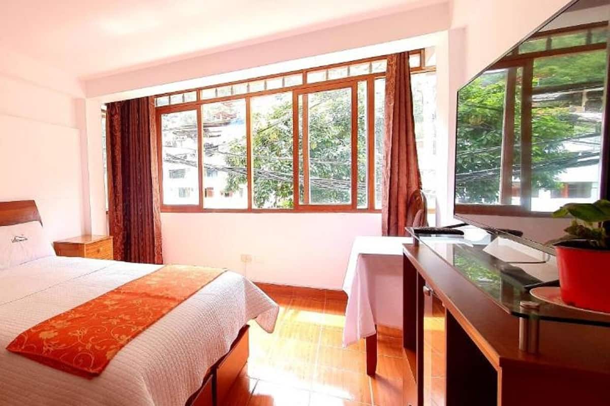 A hotel room with a bed, a desk, a window with curtains, and a small table.