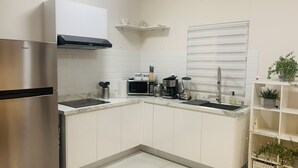 A modern kitchen with white cabinets, a stainless steel refrigerator, a microwave, a coffee maker, and a blender.