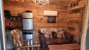 A rustic cabin interior with a wooden ceiling, a chandelier, a refrigerator, a dishwasher, a leather sofa with deer-themed pillows, a wooden coffee table, and a patterned rug. - Lazy Bear Retreat by the Creek  (Pickens)