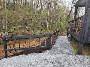 Cross a wooden bridge to a secluded pavilion surrounded by dense forest.