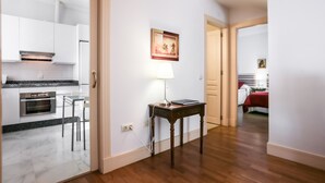 A modern kitchen with white cabinets, a marble countertop, and a built-in oven. There is a small wooden table with a lamp and a framed picture on the wall. - Garcia de Vinuesa Atico by Home at Homes (Sevilla)