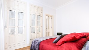 A bedroom with a wooden floor, a red bedspread, and white double doors with curtains. - Garcia de Vinuesa Atico by Home at Homes (Sevilla)