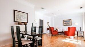 A spacious living room with a wooden floor, a dining area with a dark wooden table and chairs, and a red armchair. - Garcia de Vinuesa Atico by Home at Homes (Sevilla)
