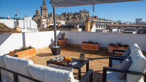 A rooftop terrace with outdoor seating, potted plants, and a view of historic architecture. - Garcia de Vinuesa Atico by Home at Homes (Sevilla)