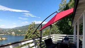 Uma varanda com toldo vermelho, com vista para um lago e colinas.