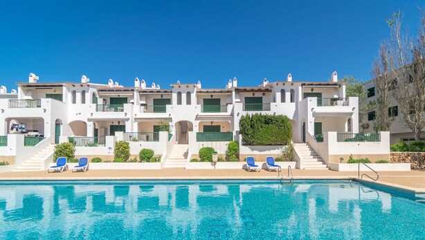 A hotel with a swimming pool, multiple balconies, and a clear blue sky. - SES FONTS C25 - Charming flat with shared pool and close to the beach. Free WiFi. (Es Mercadal)