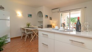 A kitchen with a dining table, chairs, a refrigerator, a window with curtains, and a bottle of wine on the counter. - SES FONTS C25 - Charming flat with shared pool and close to the beach. Free WiFi. (Es Mercadal)