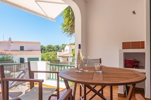 A terrace with a round wooden table, two chairs, and a bottle of champagne.