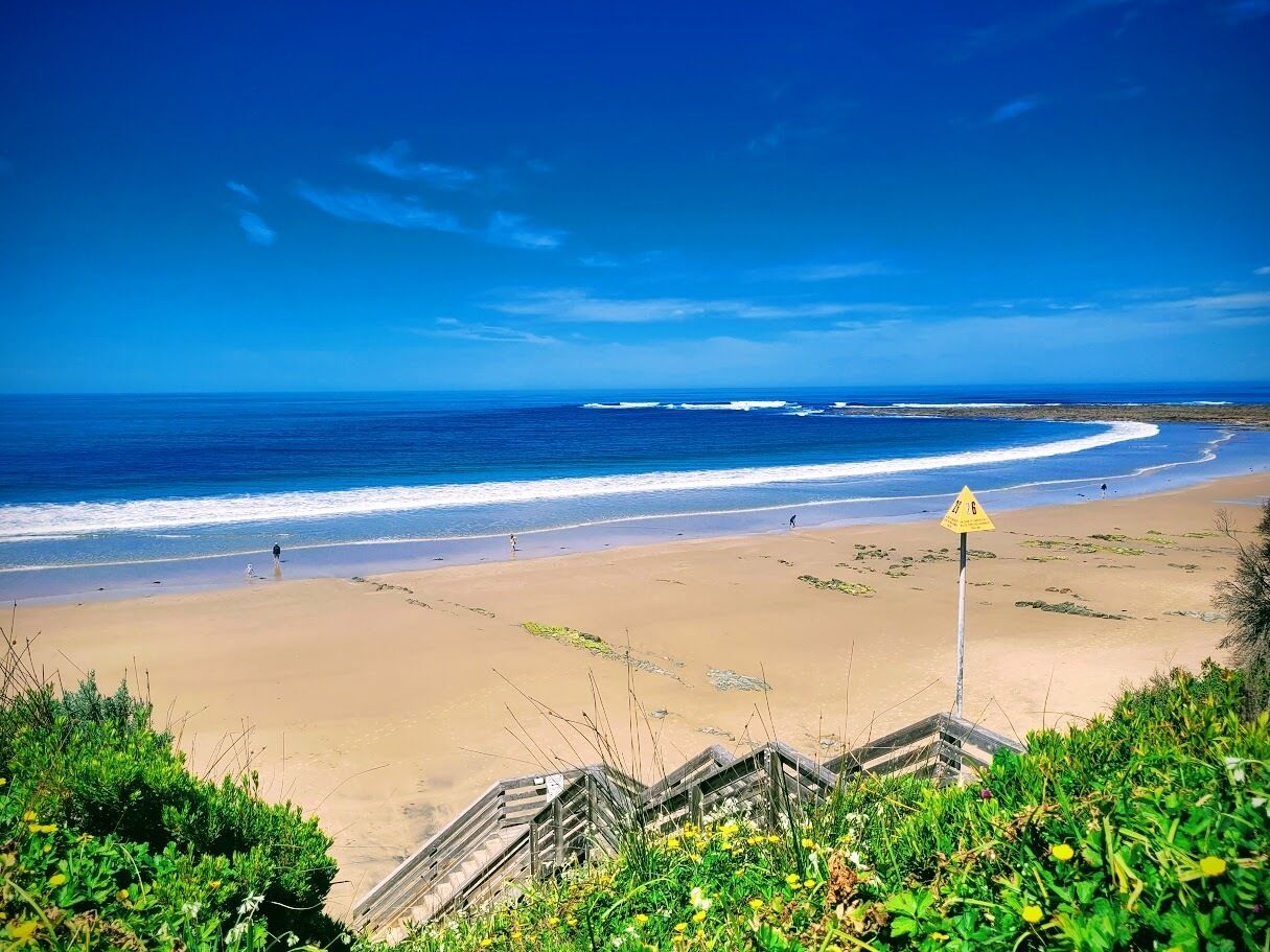 A beach with a warning sign, sandy shore, and ocean waves.