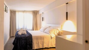 Ein Hotelzimmer mit einem Bett, einem Nachttisch, einer Lampe und einem Fenster mit Vorhängen.