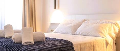 Una habitación de hotel con una cama bien hecha, una lámpara de noche y una ventana con cortinas.