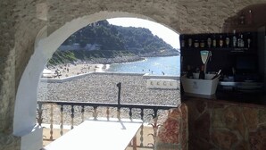 Blick auf einen Strand durch einen Rundbogen, ein Barbereich mit Flaschen und ein Schild mit der Aufschrift 'Coca-Cola'.