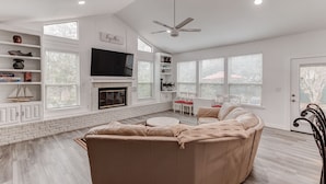 A spacious living room with a large beige sectional sofa, a fireplace, a flat-screen TV, and a ceiling fan. - Amazing! ATnT Stadium Rangers New Ball Park, Six Flags, Hurricane Harb Tex Live! (Arlington)