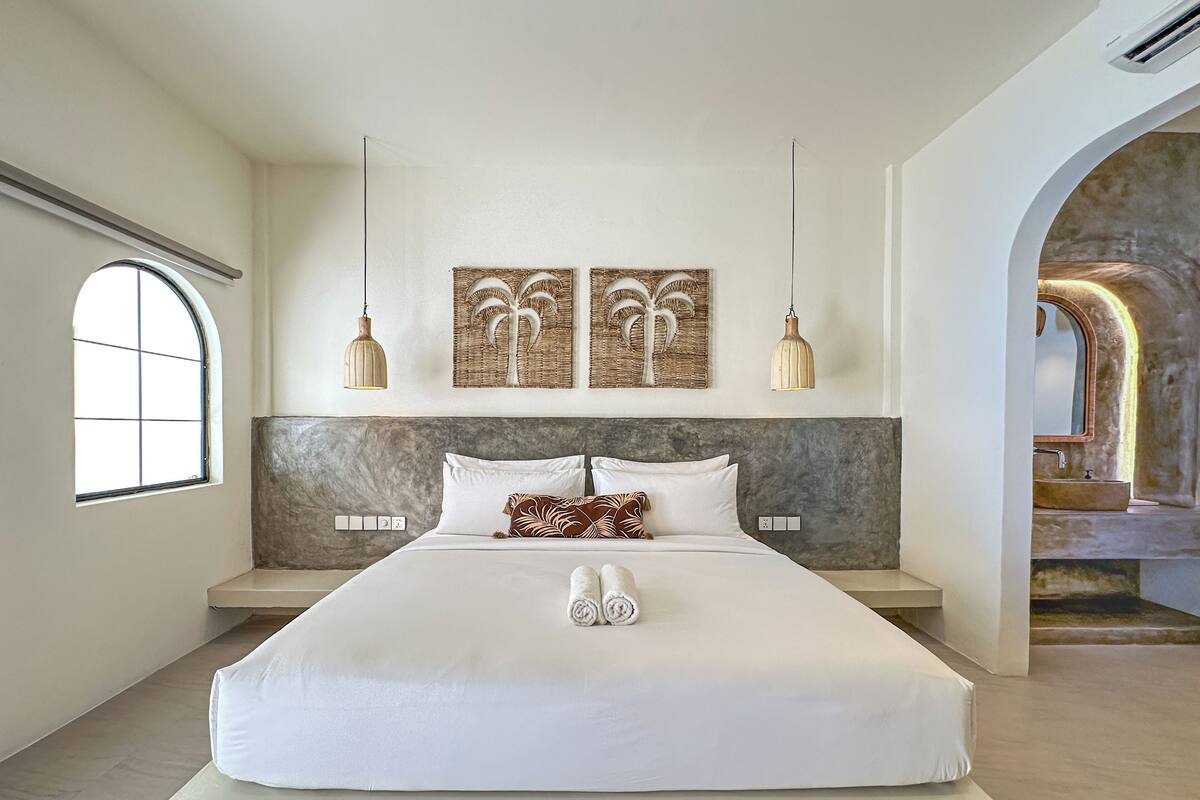 Un dormitorio moderno con una cama grande, dos lámparas colgantes fijadas a la pared, cabecera de mármol y vista a una escalera.