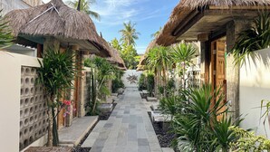 A pathway flanked by thatched-roof structures, palm trees, and a stone-tiled walkway.