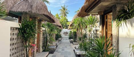 A pathway flanked by thatched-roof structures, palm trees, and a stone-tiled walkway.