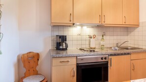 Cozinha compacta com armários de madeira, forno embutido, máquina de café e pia.
