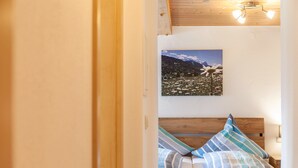 Quarto com cabeceira de madeira, cama com almofadas listradas, quadro pendurado na parede com paisagem e luminária no teto.