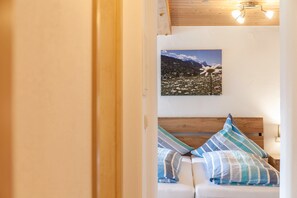 Une chambre à coucher avec une tête de lit en bois, un lit agrémenté d’oreillers à rayures, un tableau représentant un paysage accroché au mur et un luminaire fixé au plafond.