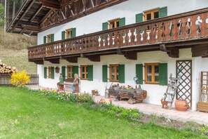 Un chalet traditionnel doté d’un balcon, de volets en bois et d’un jardin agrémenté de fleurs et de plantes.