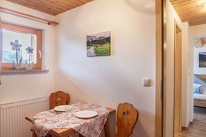 Un coin repas avec une table dressée pour deux personnes, une fenêtre décorée de fleurs et un tableau représentant un paysage accroché au mur.