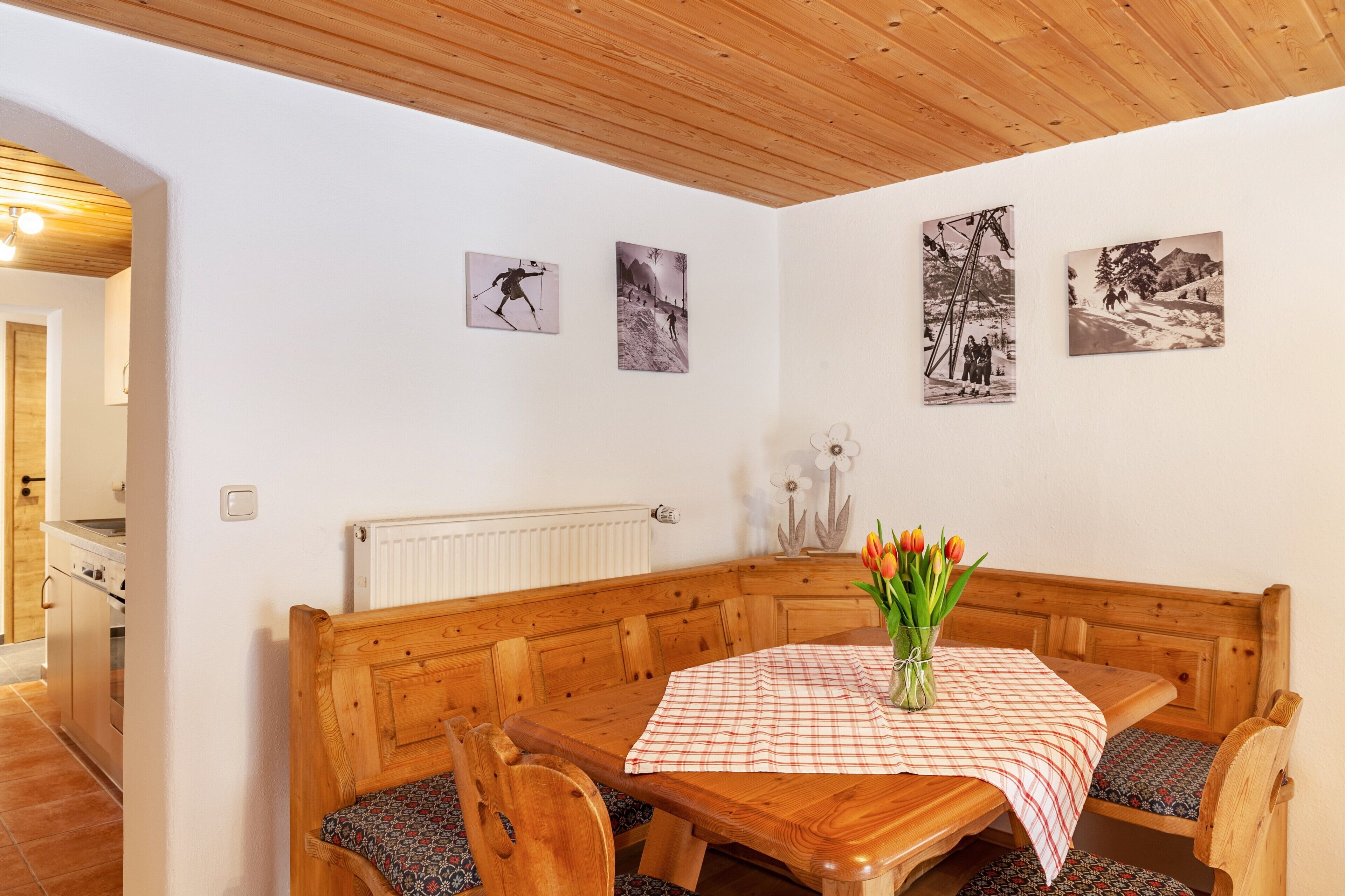 A wooden dining area with a checkered tablecloth, wooden bench seating, and a vase of tulips.
