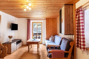 A cozy room with a wooden ceiling, a sofa, a television, and a window with curtains.