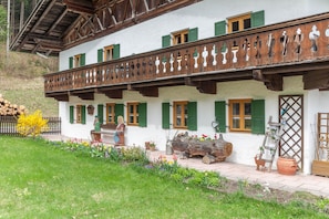 A traditional chalet with a balcony, wooden shutters, and a garden with flowers and plants.
