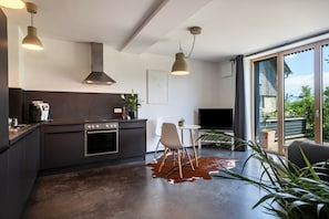 A modern kitchen with dark cabinetry, a stove, and a dining area with a cowhide rug. - Apartment 'La Casa Nel Verde' with Green Views, Private Terrace & Wi-Fi (Lindau)