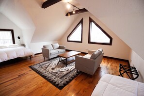 A spacious loft bedroom with a large bed, a sofa, a coffee table, and two windows providing natural light.