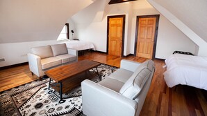 Camera in stile loft con soffitto spiovente, trave in legno, due porte di legno, un letto bianco, un divano bianco, un tavolino in legno e un tappeto a motivi.