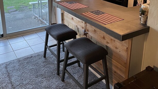 A kitchen with a bar area, two stools, a refrigerator, and a coffee maker.